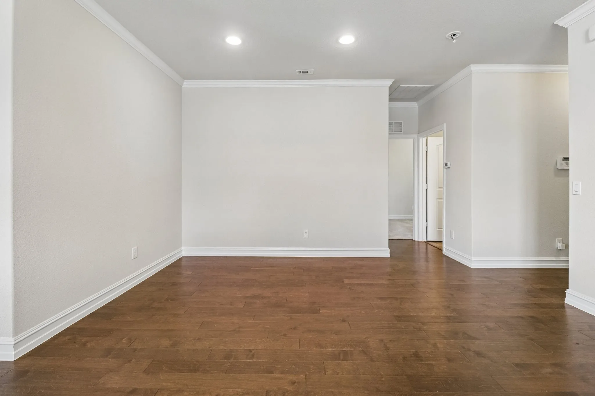 Recessed lighting illuminates the wood-finish flooring and crown molding