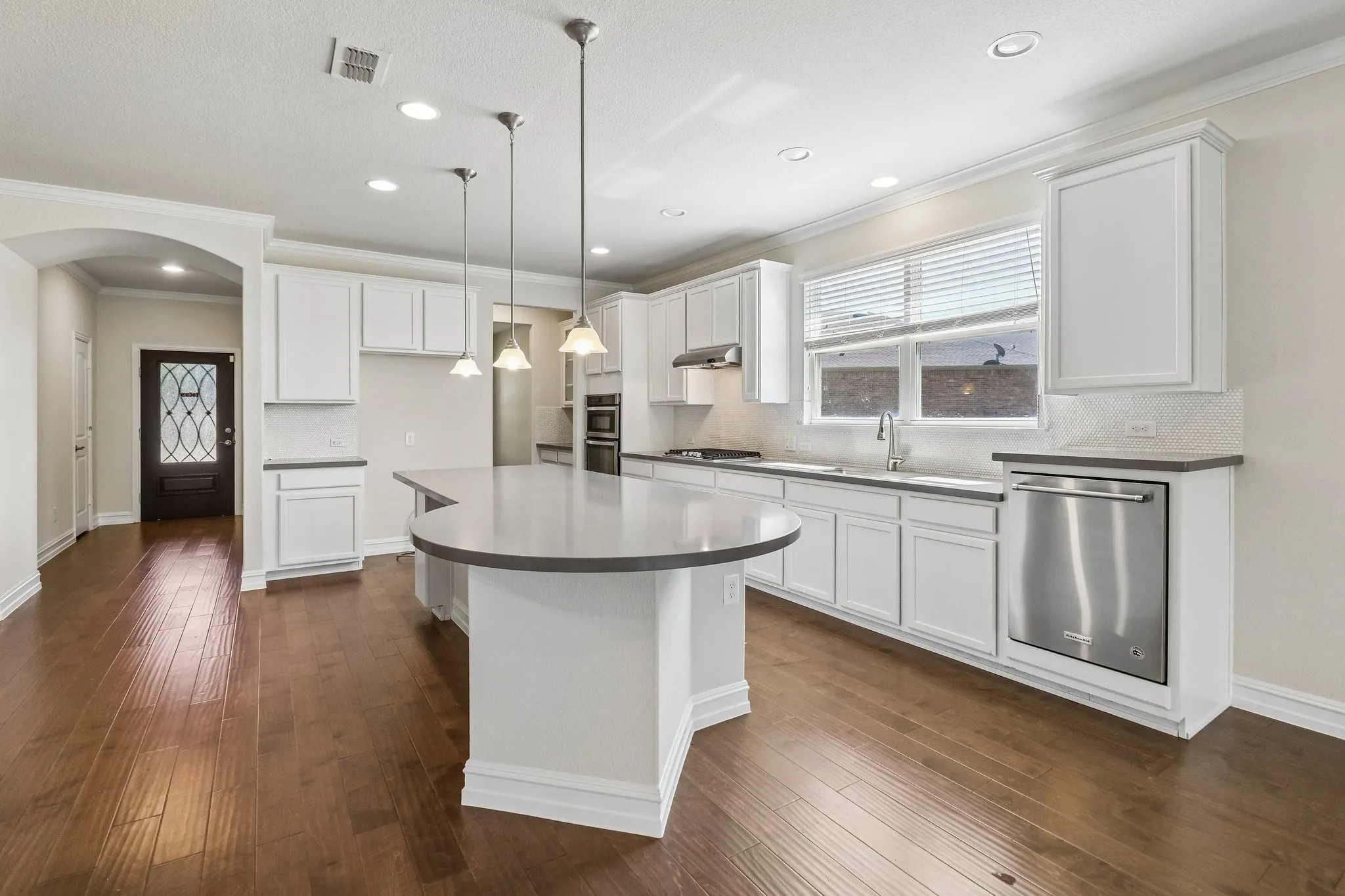 Kitchen featuring wood-finish flooring, an expansive island with a light-toned countertop, white cabinetry, stainless steel appliances, and recessed lighting