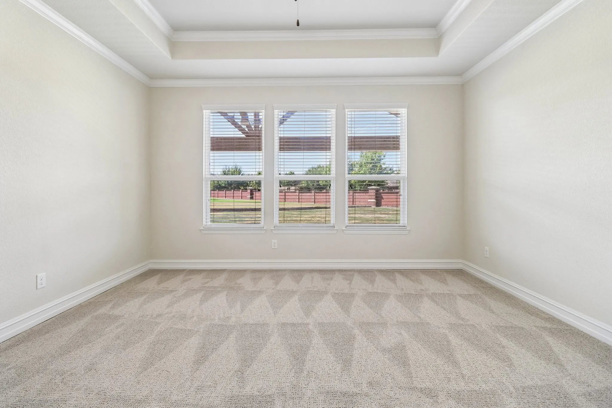 Recessed ceiling with crown molding, three large windows, and neutral carpeting