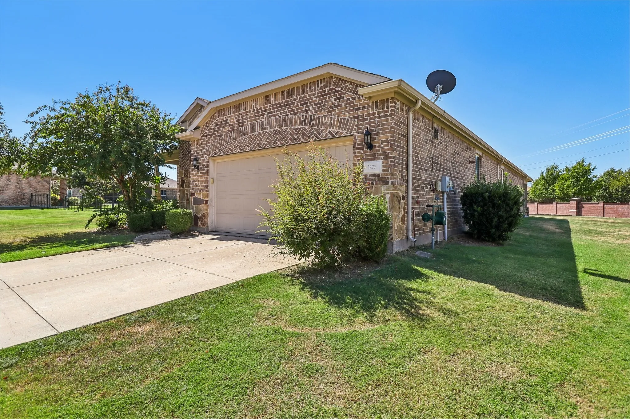 Brick exterior with an arched garage door, concrete driveway, and established landscaping