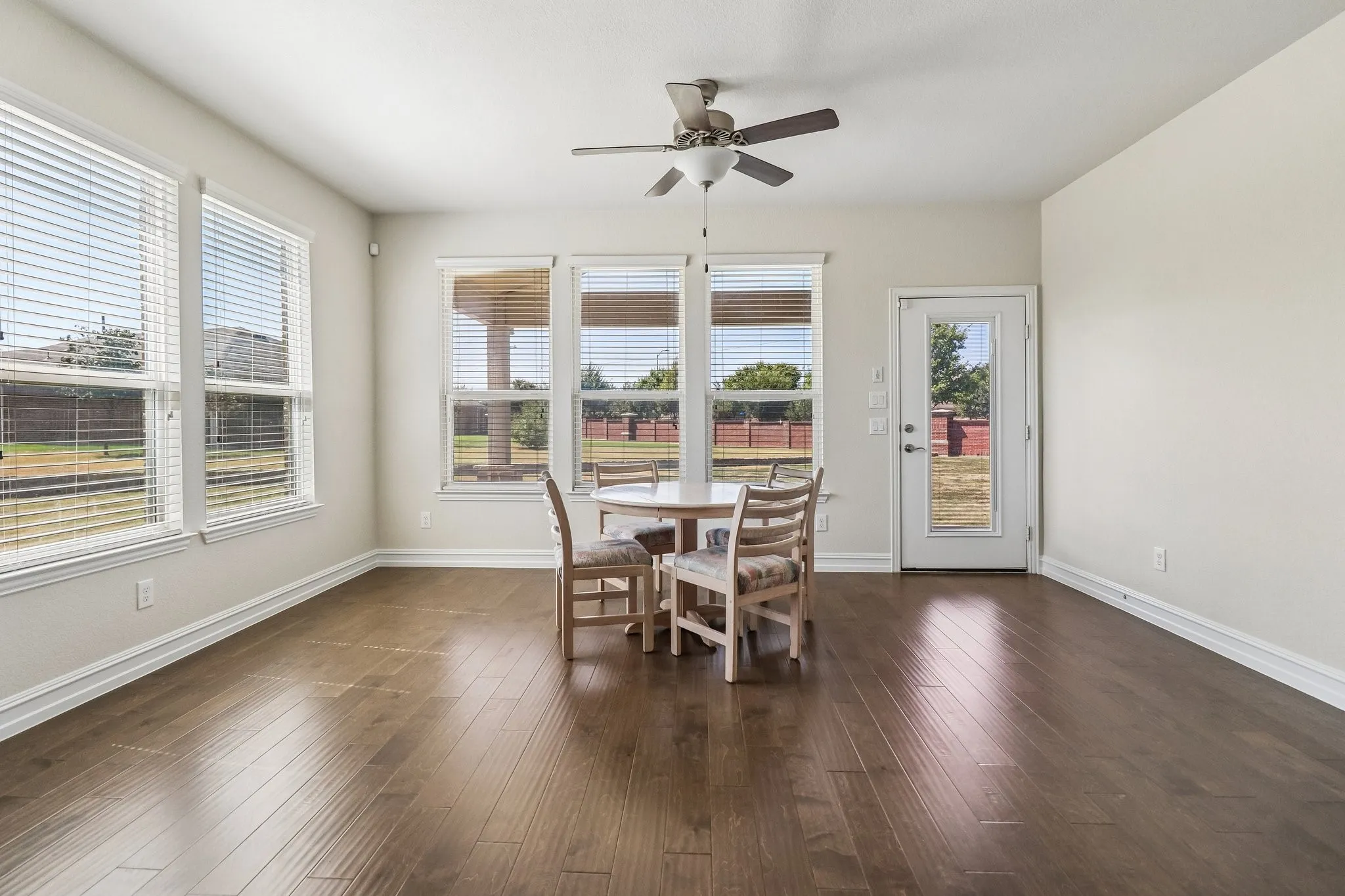 Wood-finish flooring throughout, multiple windows with blinds, ceiling fan, and a glass-paneled exterior door
