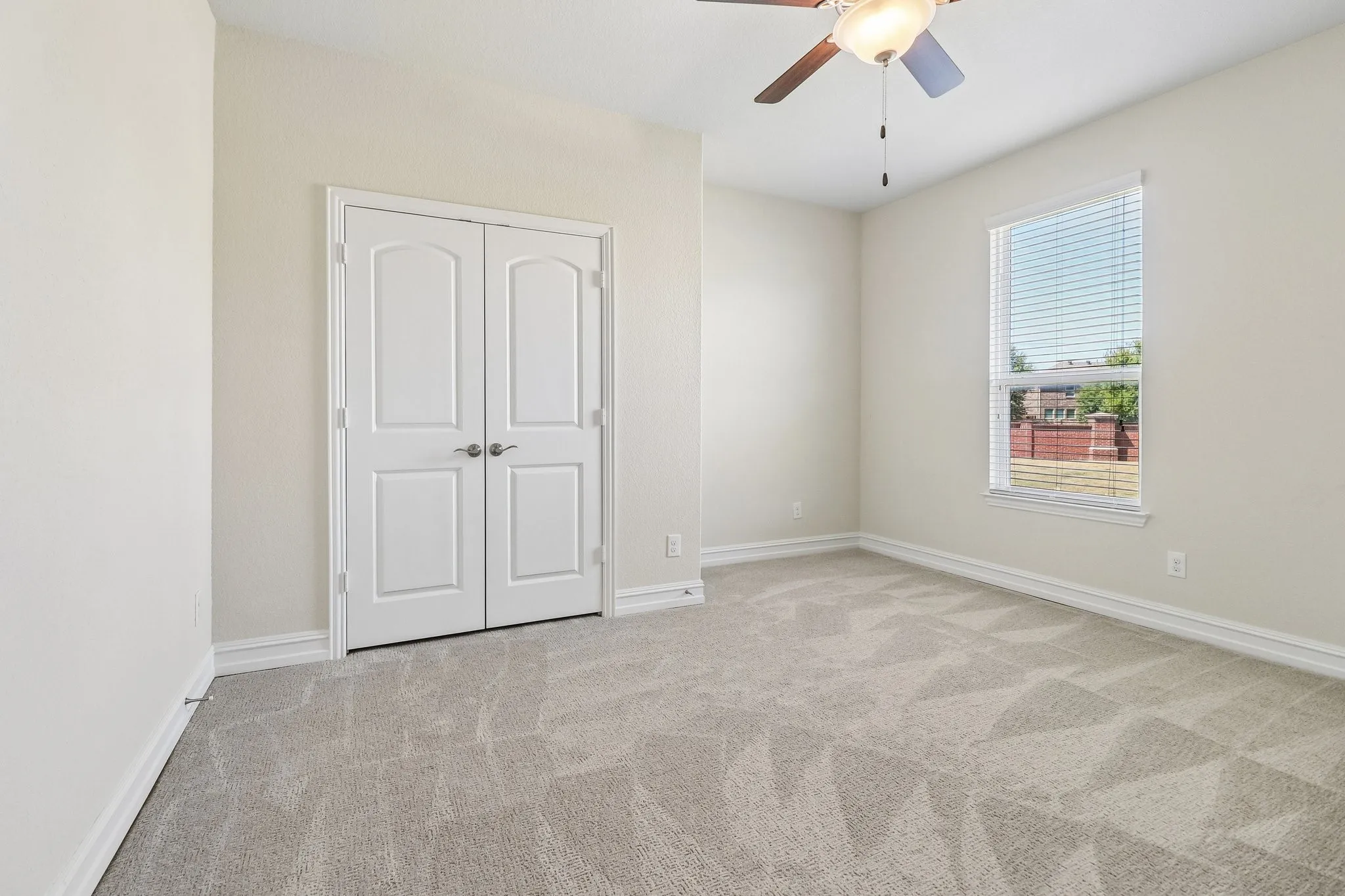 Neutral wall color, ceiling fan with integrated lighting, window with blinds, light-toned patterned carpeting, and double panel doors