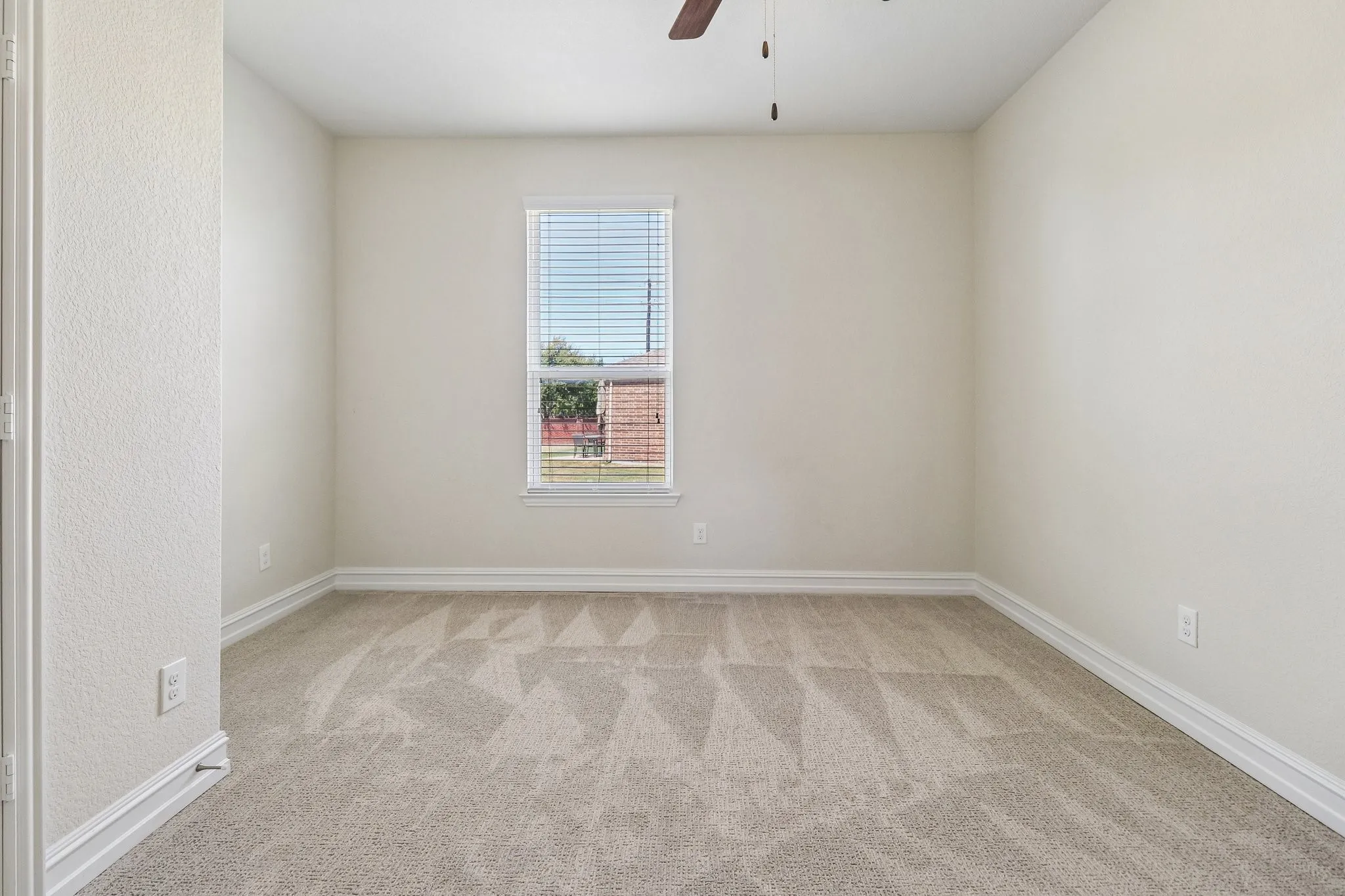 Neutral wall color, window with blinds, overhead ceiling fan, and patterned carpeting