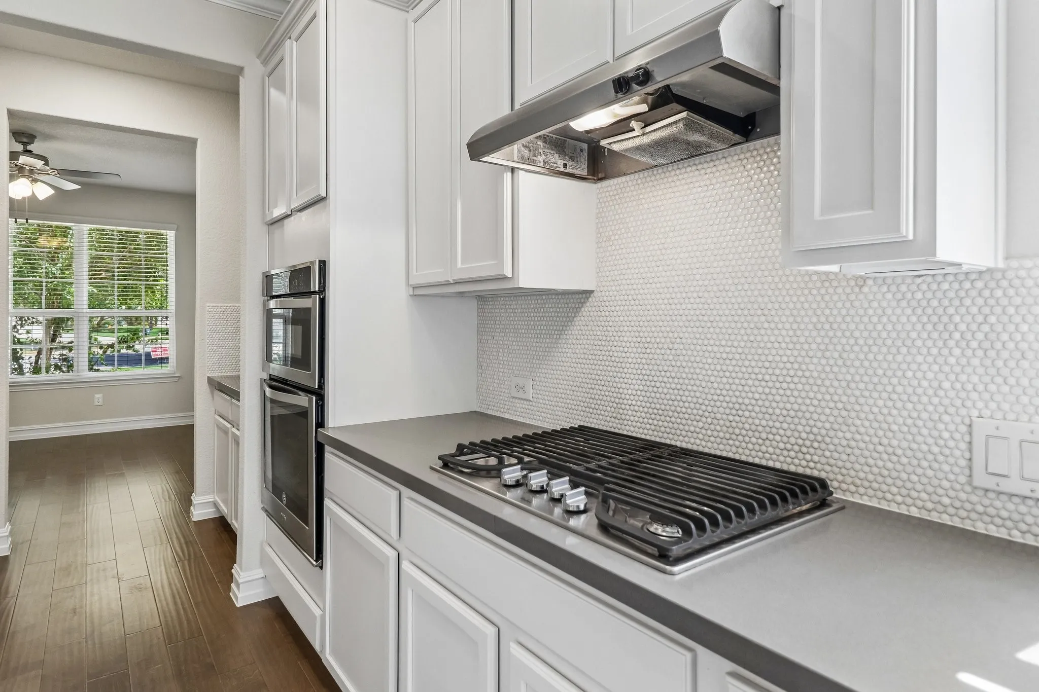 White shaker cabinetry, stainless steel double wall ovens, gas cooktop, and a penny tile backsplash