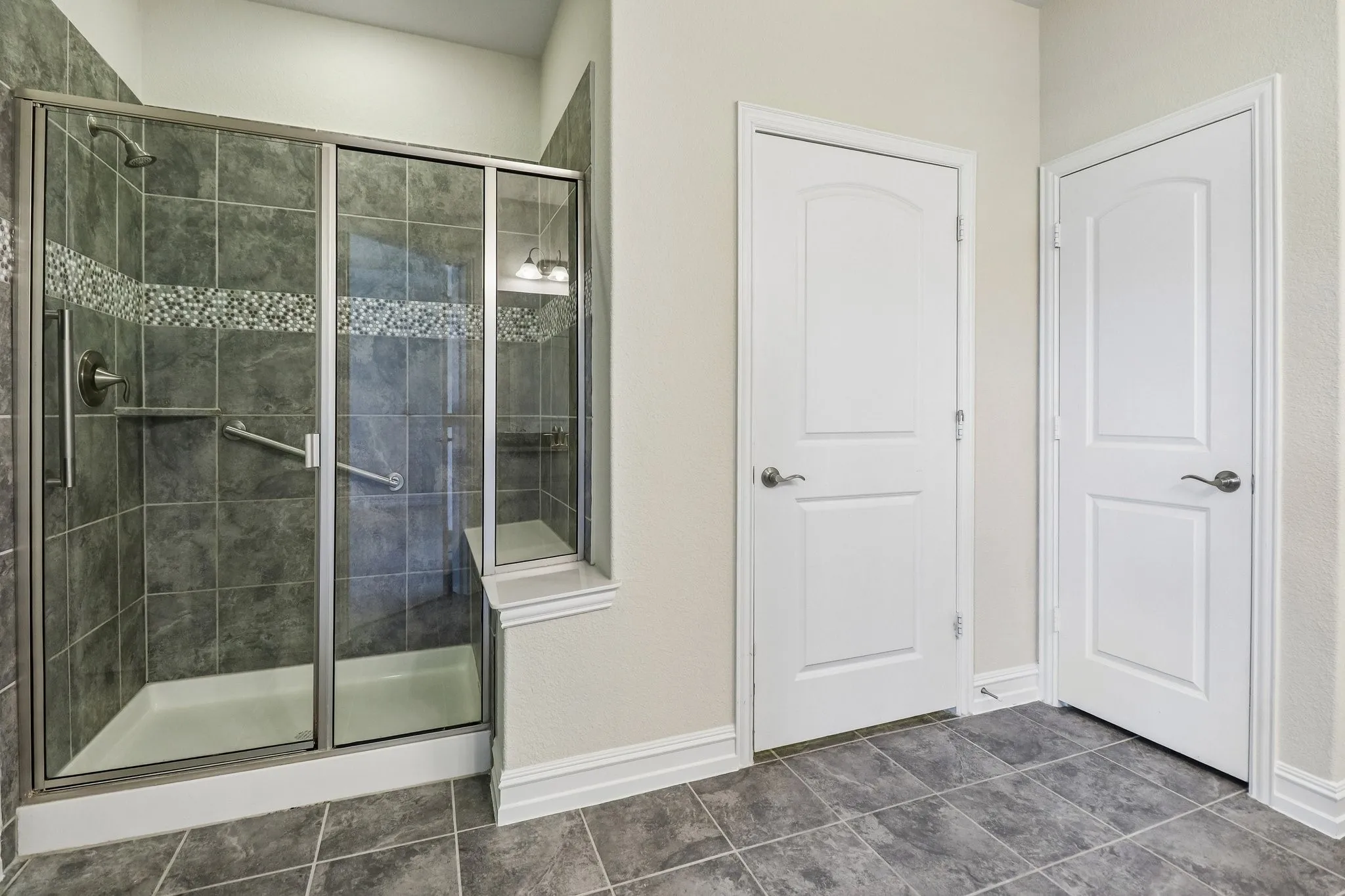 Walk-in shower with glass enclosure, dark tile surround, decorative mosaic accent, and built-in bench
