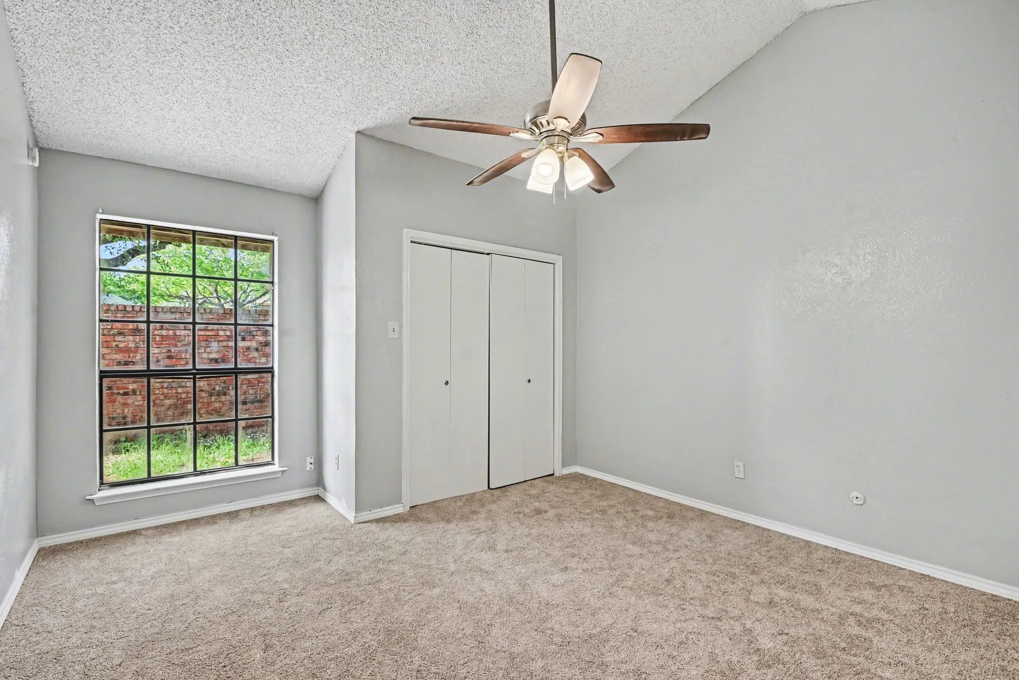 Vaulted ceiling with a ceiling fan, carpet flooring, a multi-pane window, and bifold closet doors