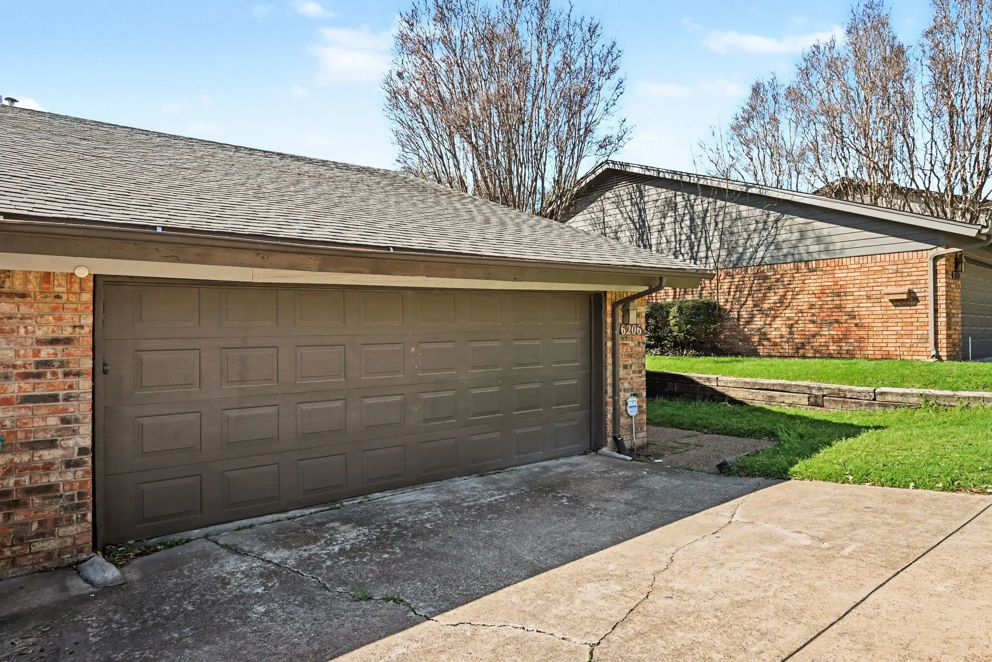 Attached garage with paneled door, brick exterior, and a concrete driveway