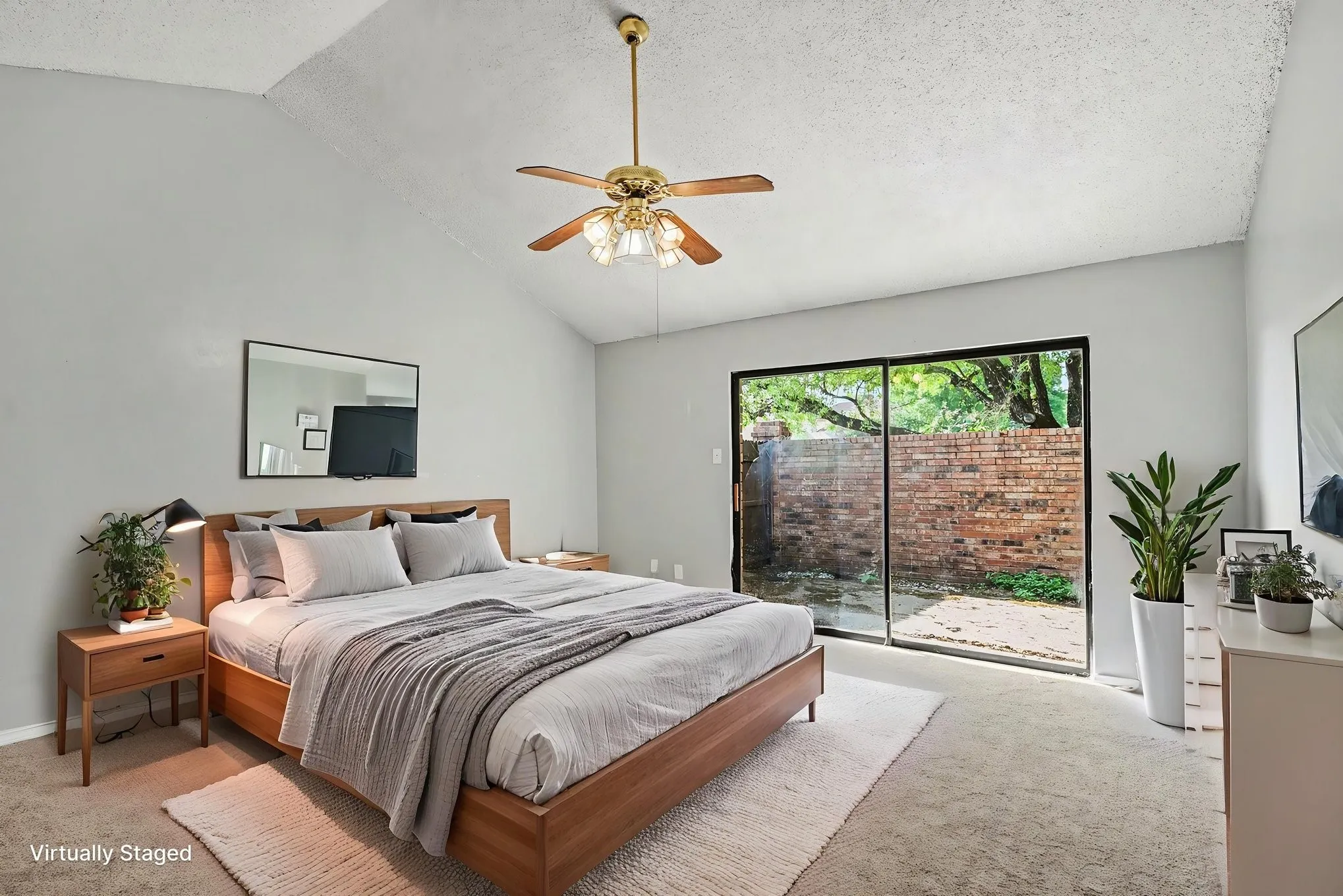 Vaulted ceiling with an attached ceiling fan, light gray wall paint, and a sliding glass door to an outdoor area with a brick wall