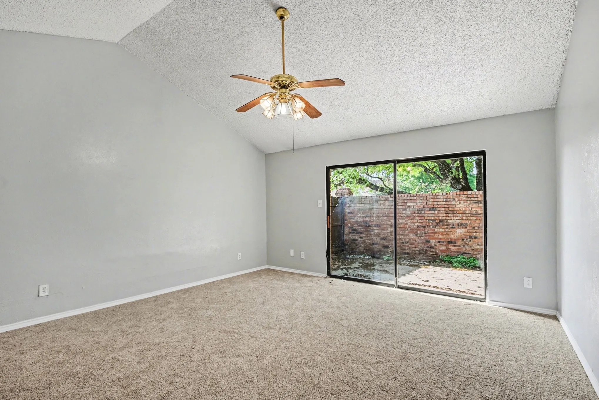 Vaulted ceiling, ceiling fan with light fixture, carpeted flooring, sliding glass door, and brick hardscaping