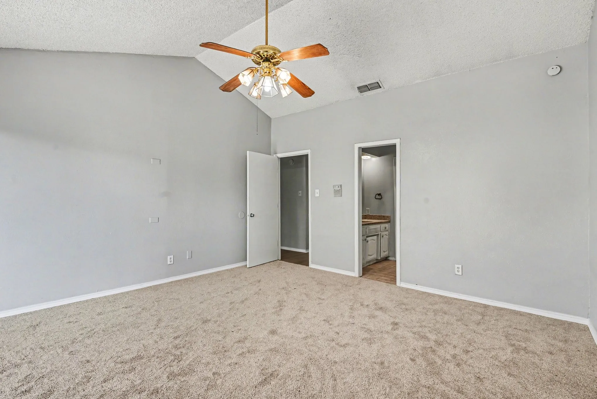 Vaulted ceiling with a brass-finish ceiling fan, neutral carpeting, and light gray wall paint