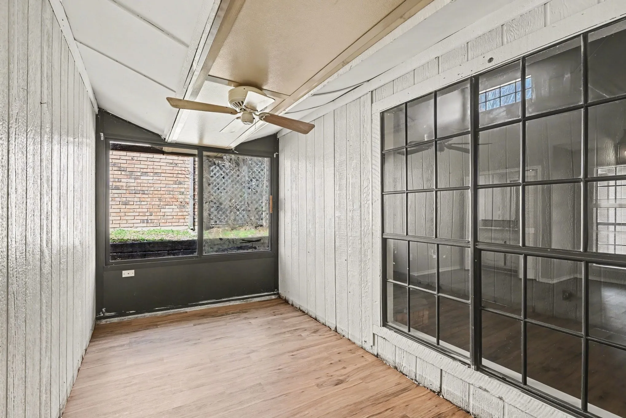 Enclosed porch with wood-finish flooring, white paneled walls, and a ceiling fan