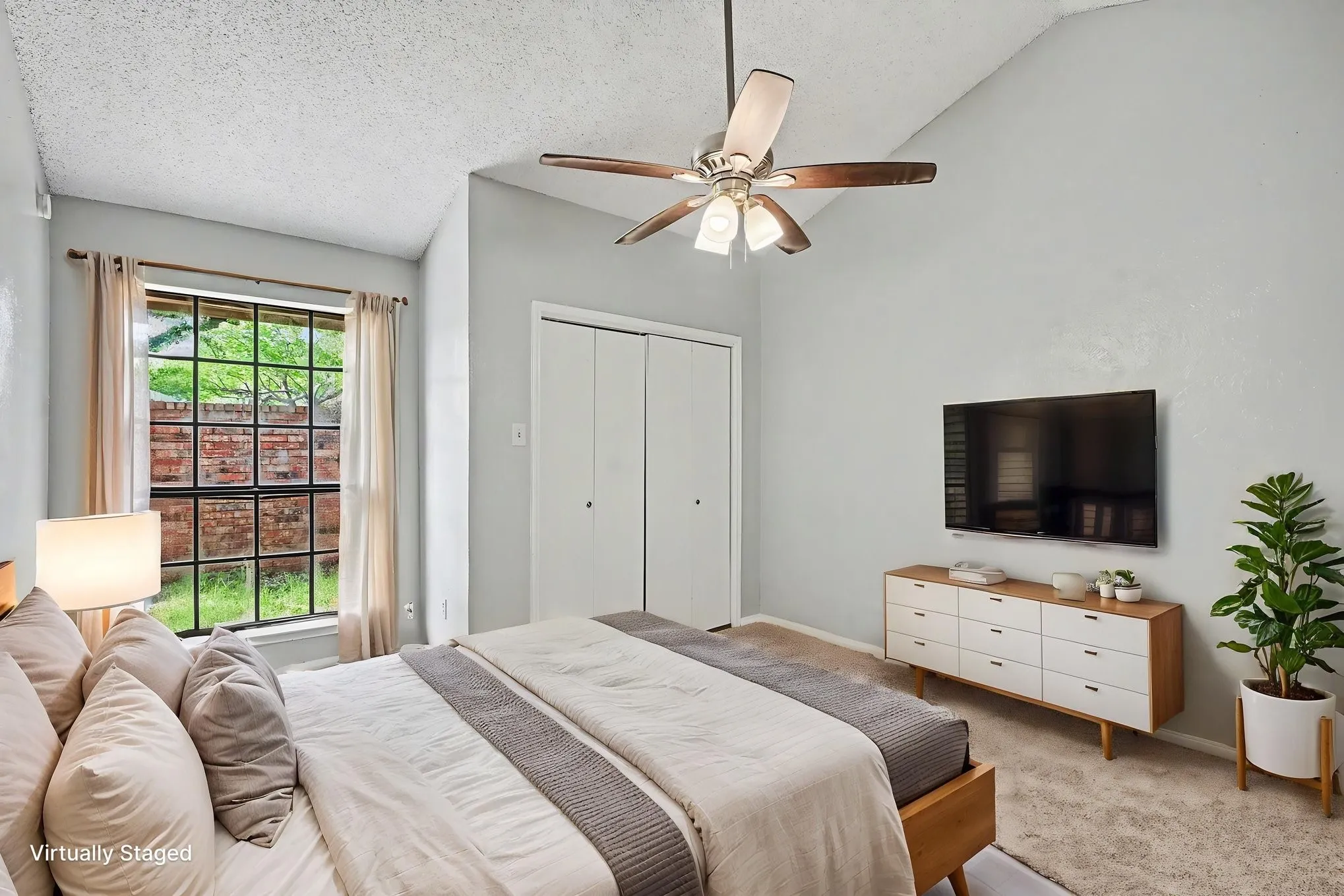 Vaulted ceiling, ceiling fan with integrated lighting, large multi-pane window, bi-fold closet doors, and neutral wall tones