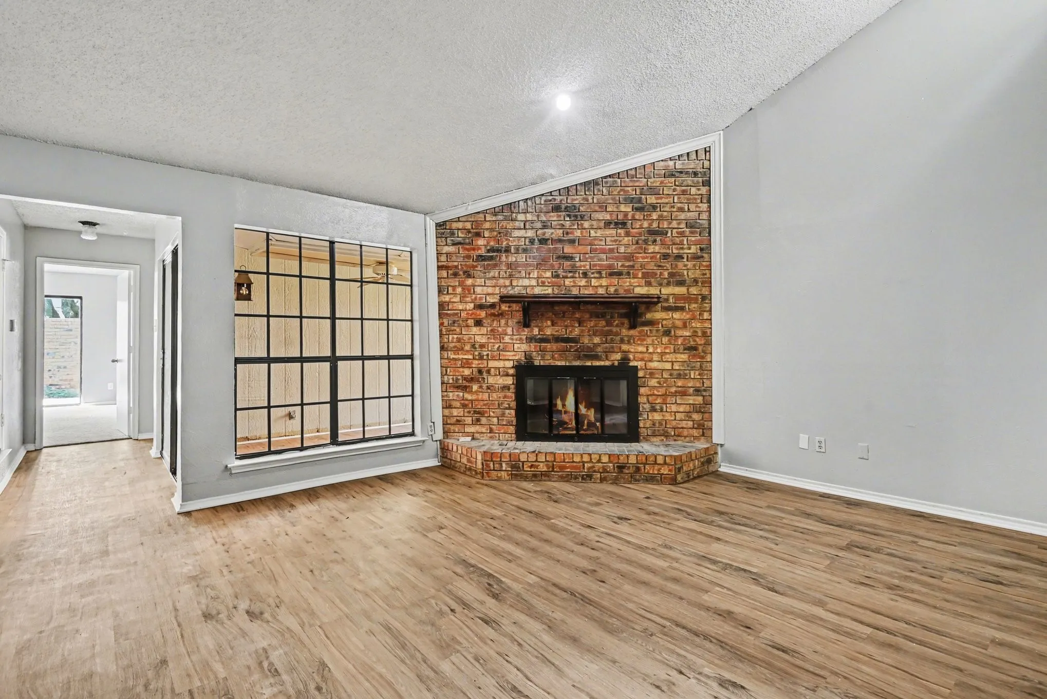 Brick fireplace with a hearth, wood-finish flooring, and a large grid window