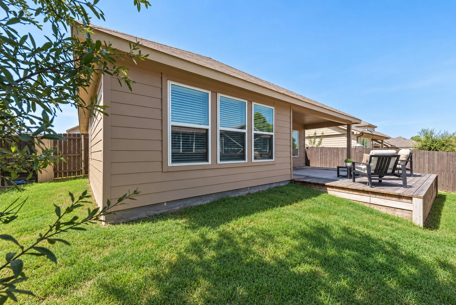 Expansive grassy yard with a wooden privacy fence, a raised wooden deck, a covered patio, and multiple windows with blinds