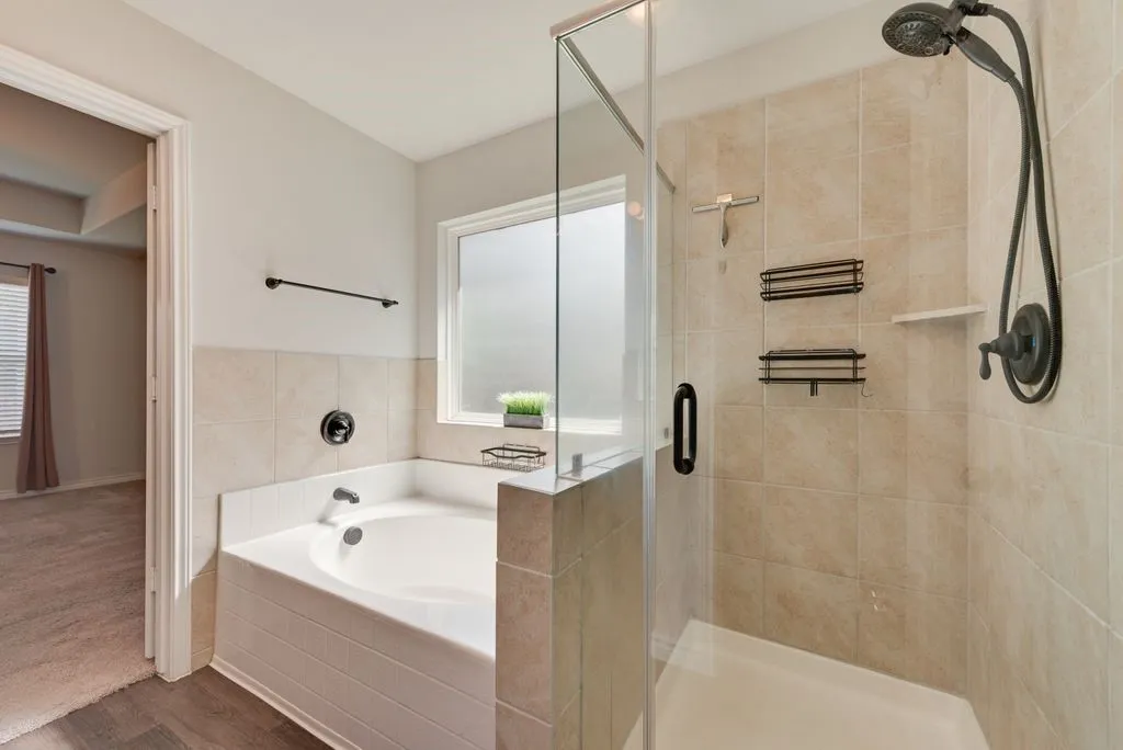 Tiled shower with glass enclosure, separate soaking tub, and a window for natural light