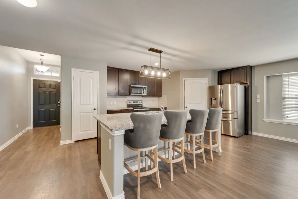 Open-concept kitchen featuring dark wood cabinetry, stainless steel appliances, granite countertops, and an island with seating