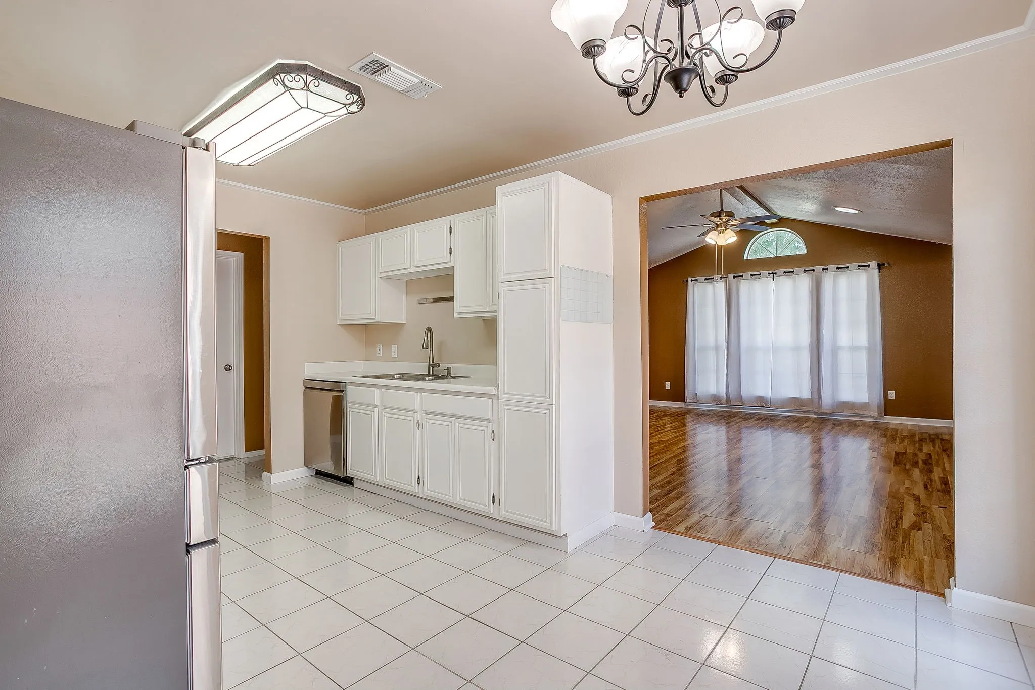 Kitchen featuring white cabinetry, stainless steel dishwasher, tile flooring, and integrated lighting, with wood-finish flooring in the secondary space