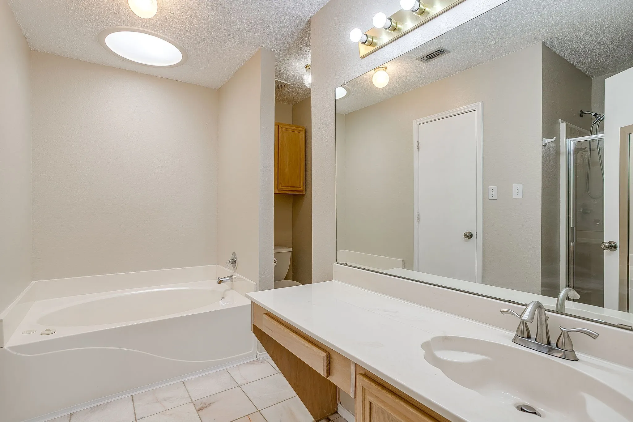 Bathroom featuring a deep soaking tub, a large vanity with a solid-surface countertop and integrated sink, a full-width wall mirror, tile flooring, and a circular skylight