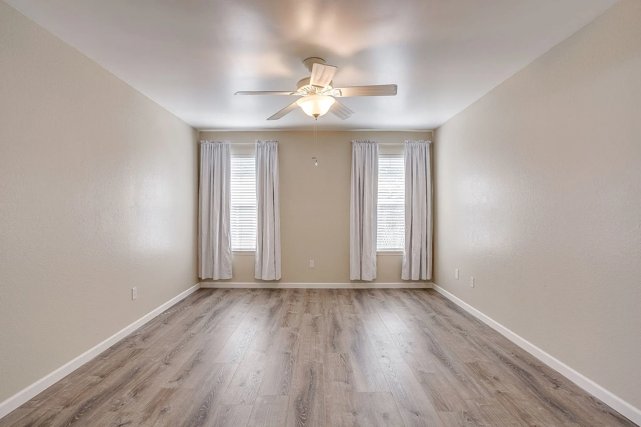 Room featuring wood-finish flooring, dual windows with blinds, and a centrally mounted ceiling fan with integrated light fixture