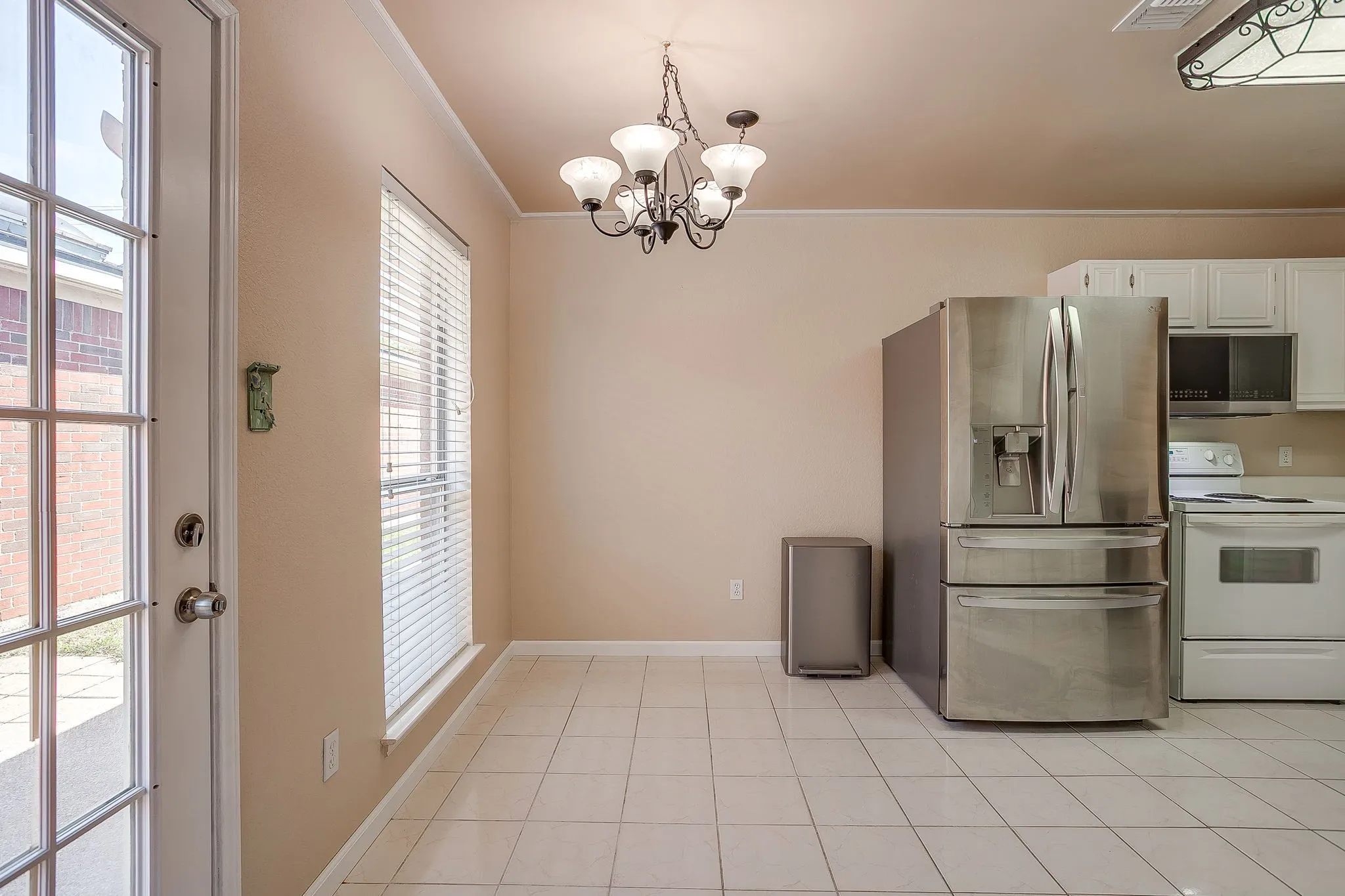 Kitchen featuring ceramic tile flooring, a multi-arm chandelier, white upper cabinetry, stainless steel French-door refrigerator, and a glass-paneled exterior door