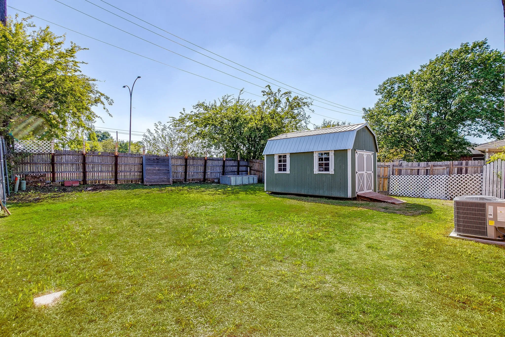 Backyard featuring a grass lawn, standalone storage building with a metal roof, and wood privacy fencing with lattice accents