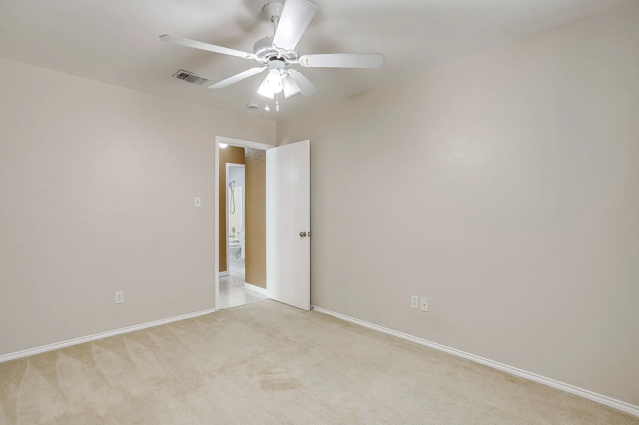 Neutral-toned interior space featuring light-colored wall-to-wall carpeting, a white ceiling fan with integrated lighting, and a six-panel door