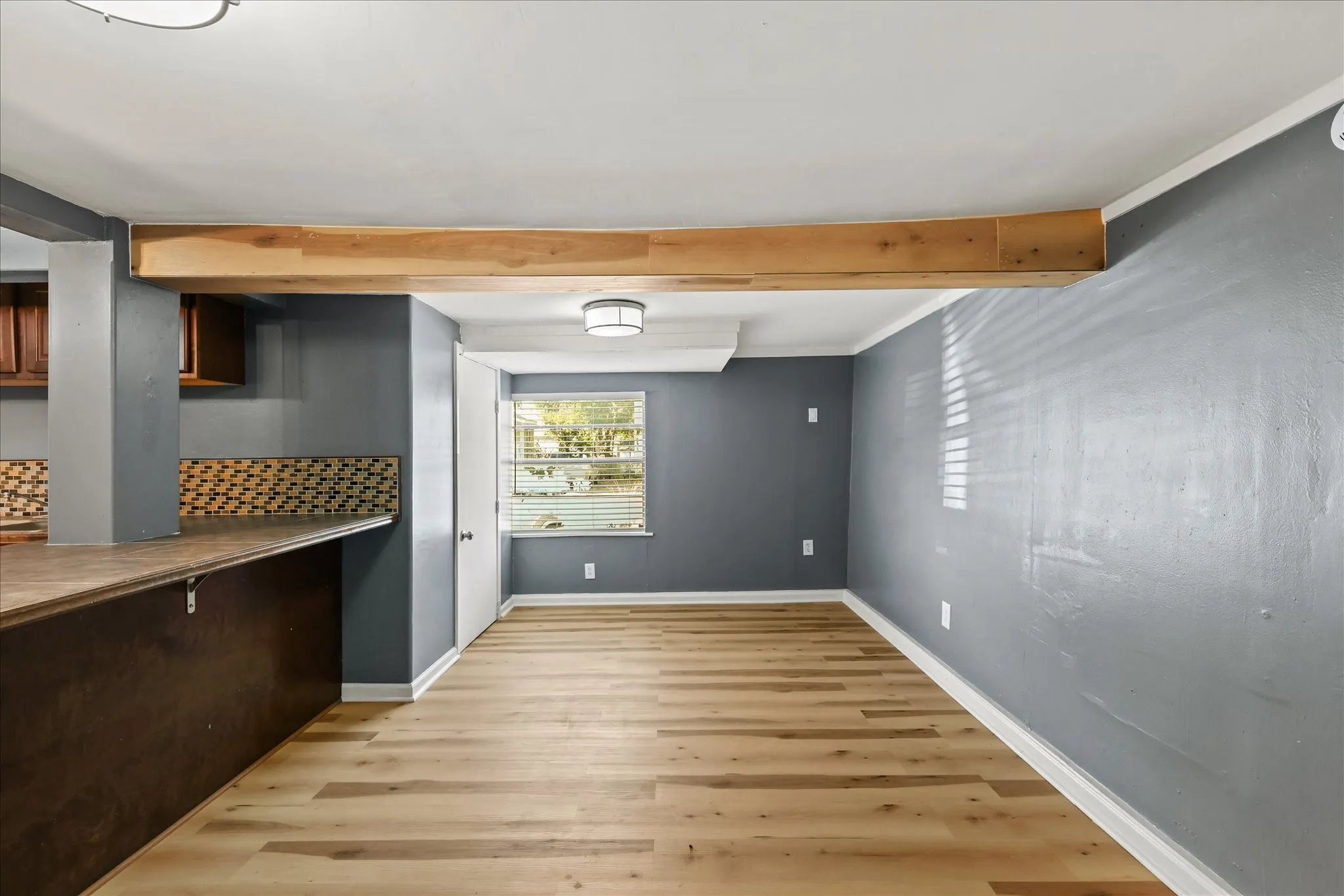 Wood-finish flooring with white baseboards, a breakfast bar with patterned tile backsplash, and a modern ceiling light fixture