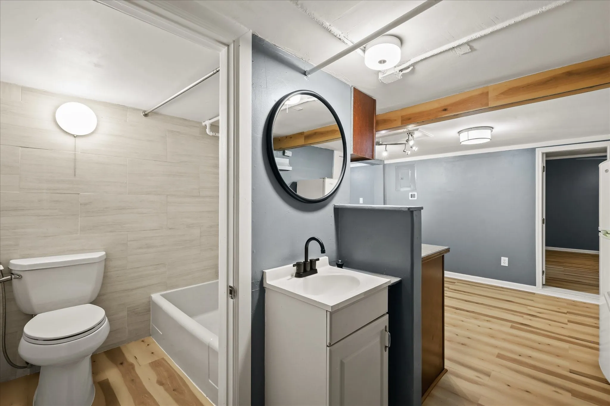 Modern bathroom featuring a white vanity with a black faucet, a round wall-mounted mirror, and light-colored tile shower surround