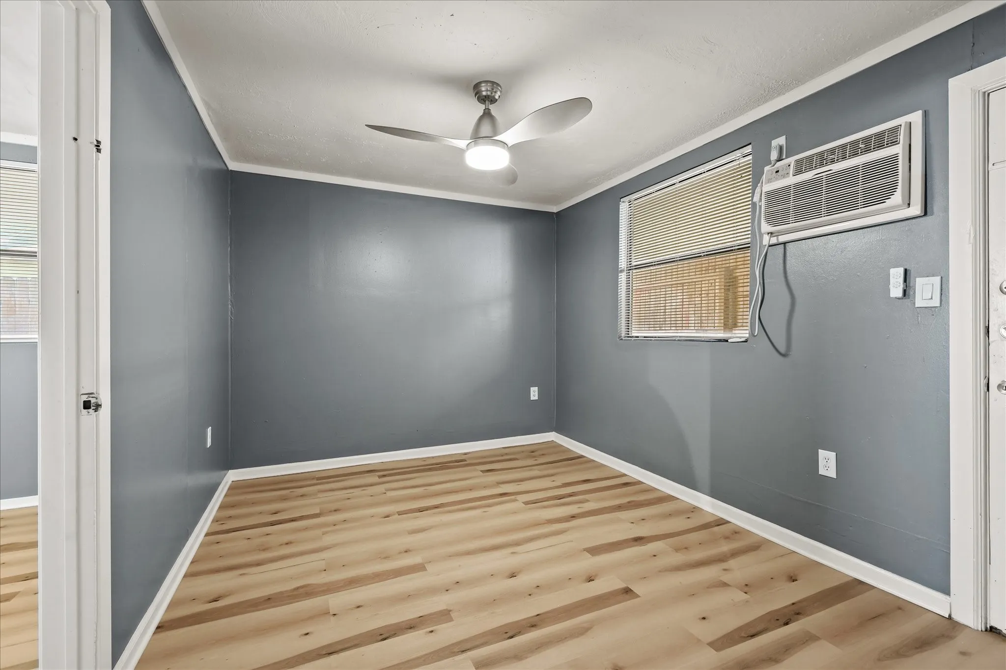 Wood-finish flooring, neutral wall paint, and a ceiling fan with integrated lighting