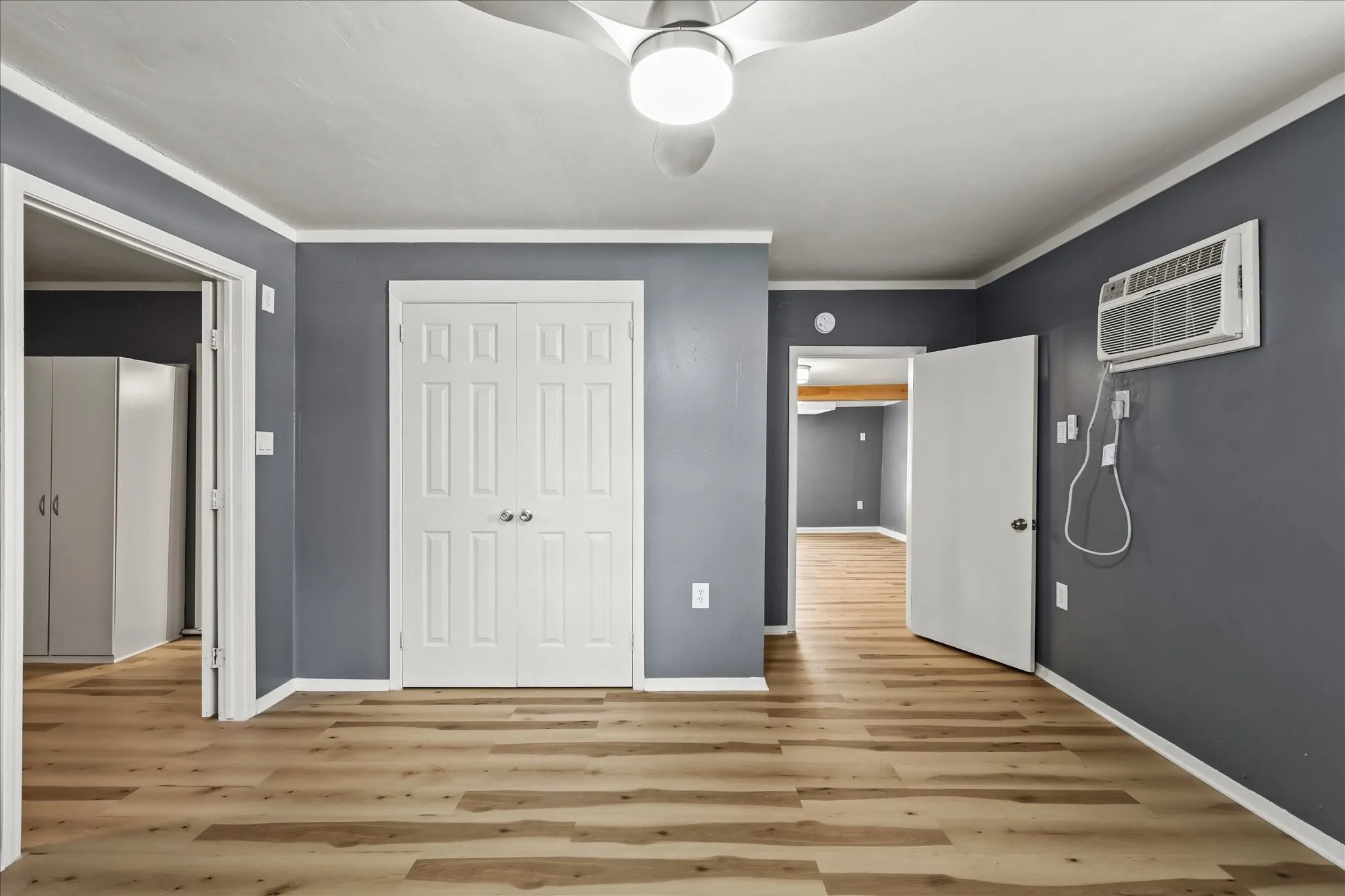 Wood-finish flooring, ceiling fan, white trim, and a built-in air conditioning unit