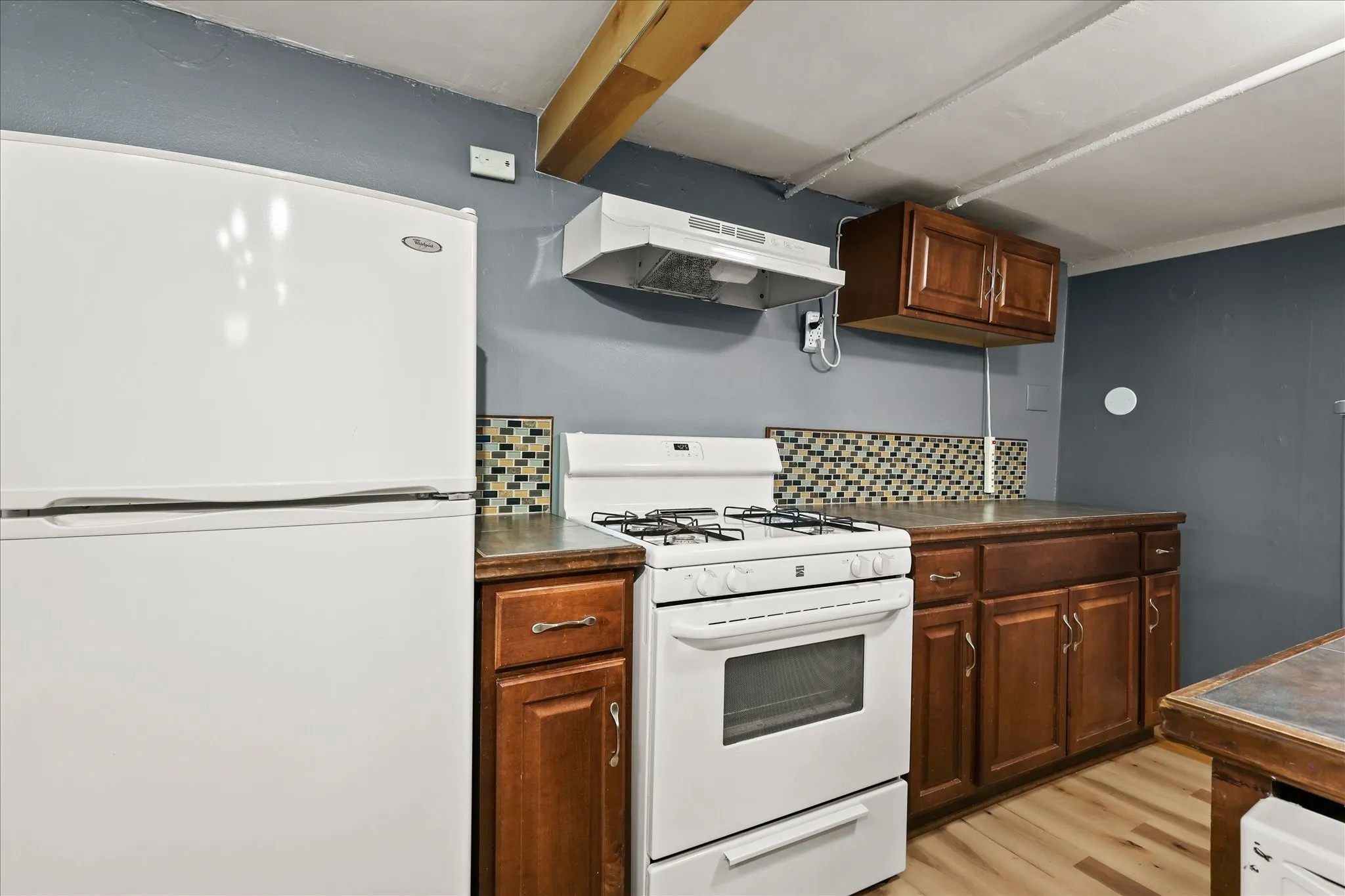 Kitchen featuring wood-finish flooring, wood cabinetry, built-in range, mosaic tile backsplash, and a white refrigerator