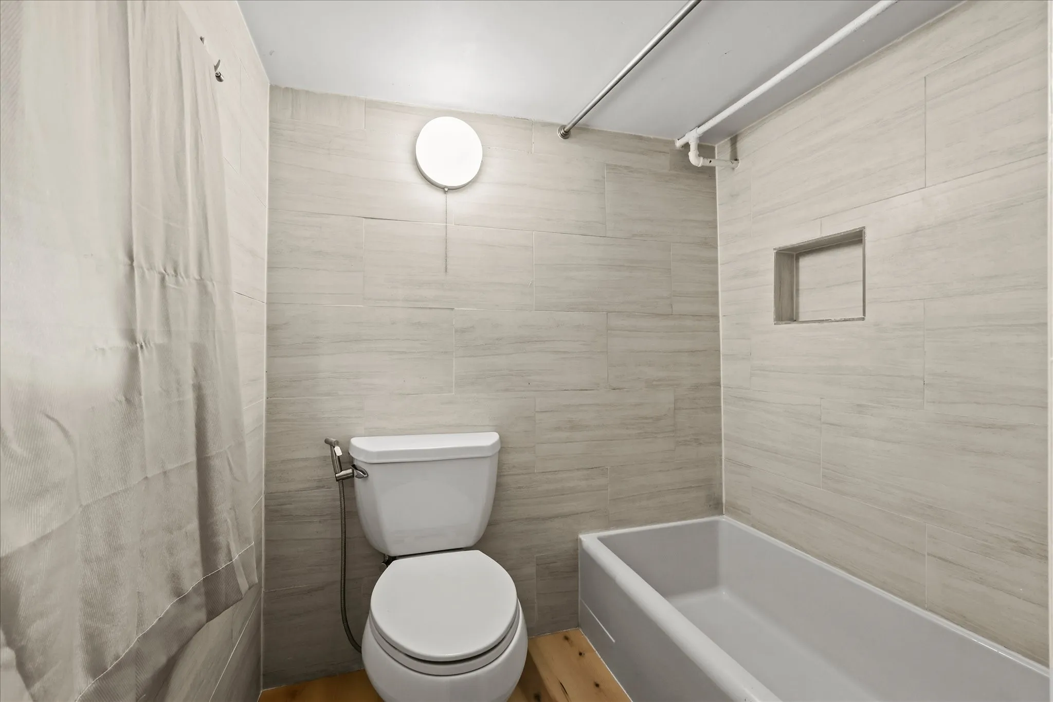 Full-height tiled walls, recessed shower niche, and a white soaking tub