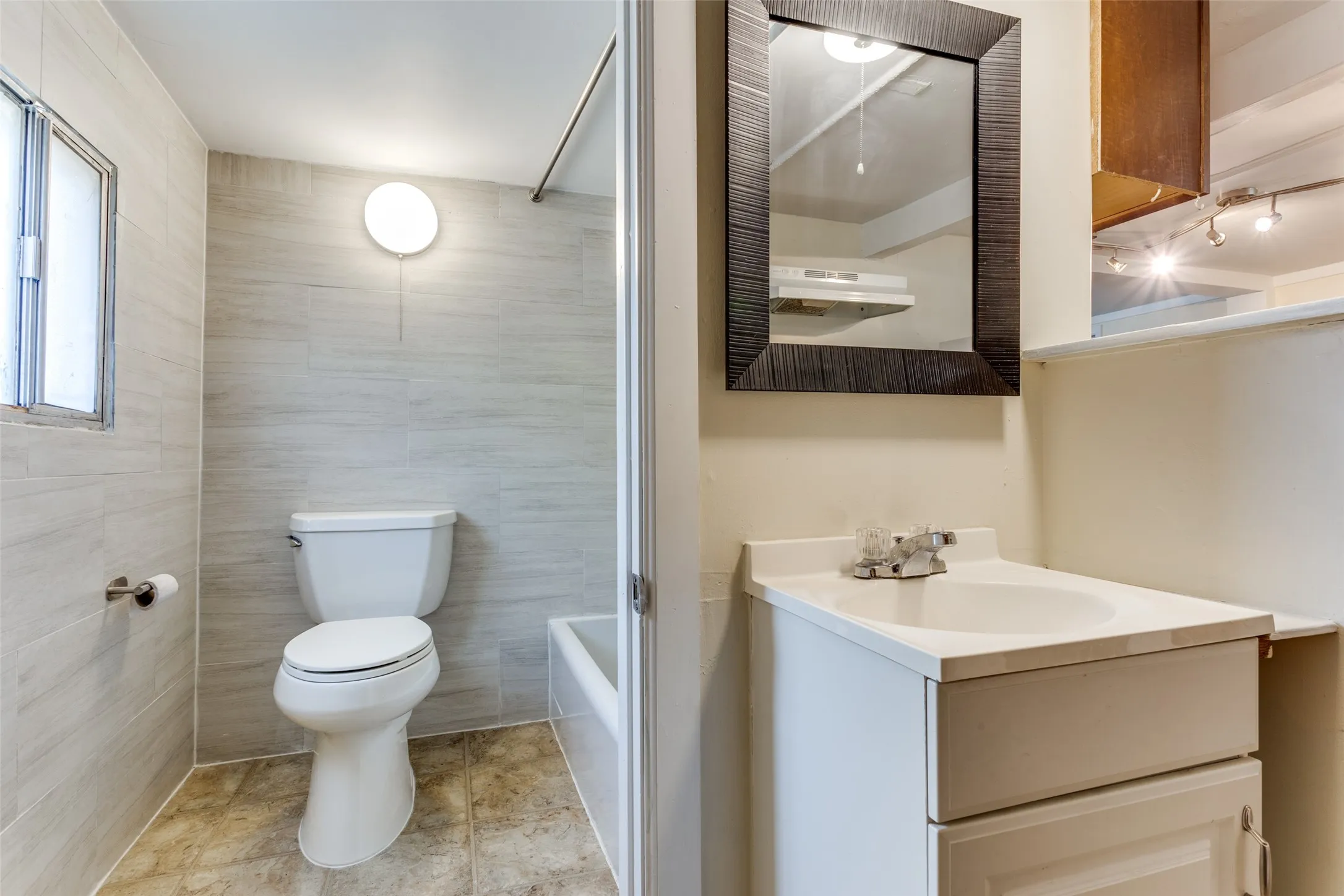 White vanity with integrated sink, framed mirror, and tiled shower surround with window