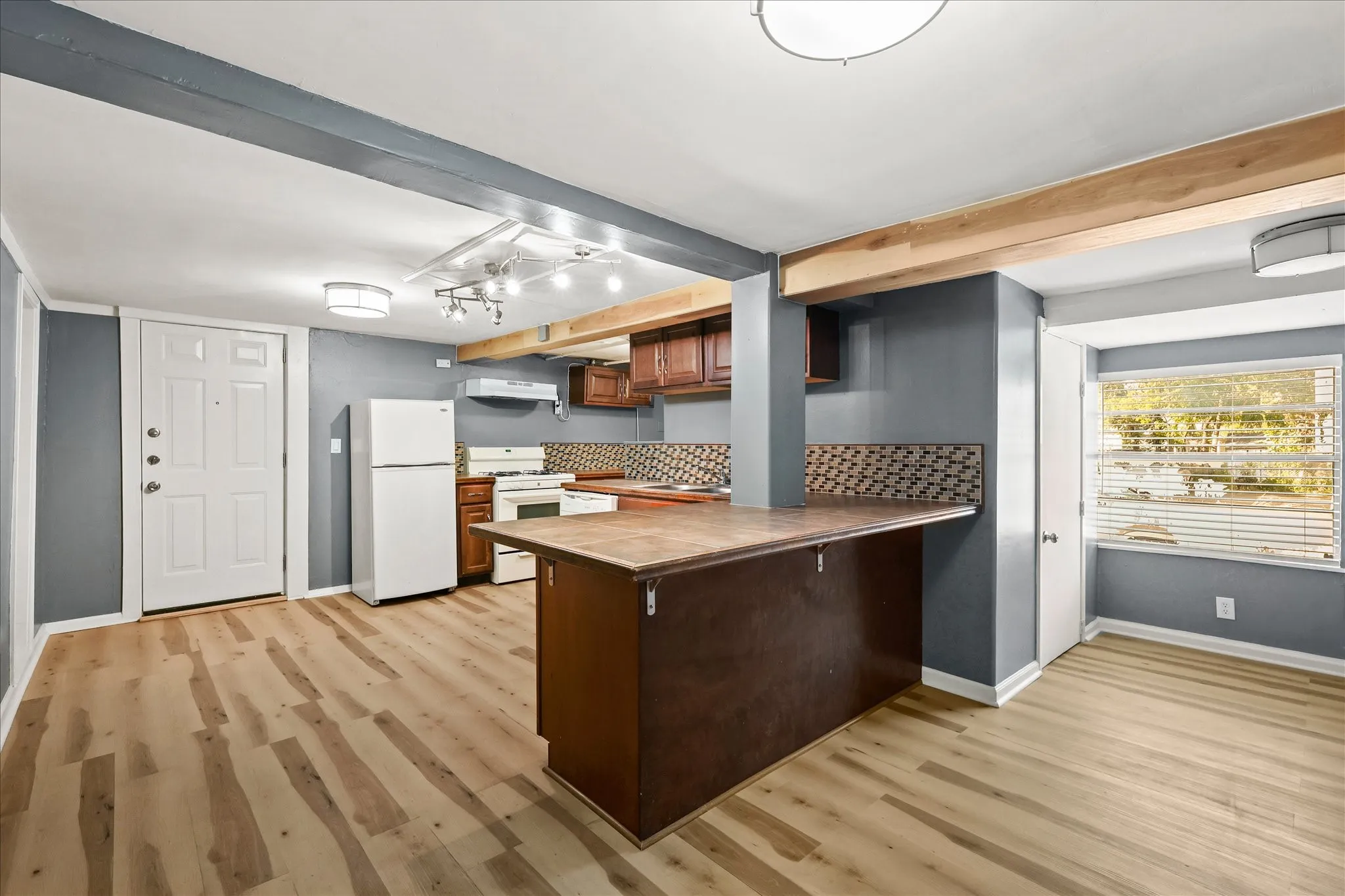 Open-concept living area featuring wood-finish flooring, exposed ceiling beams, a breakfast bar, and a kitchen with wood cabinetry