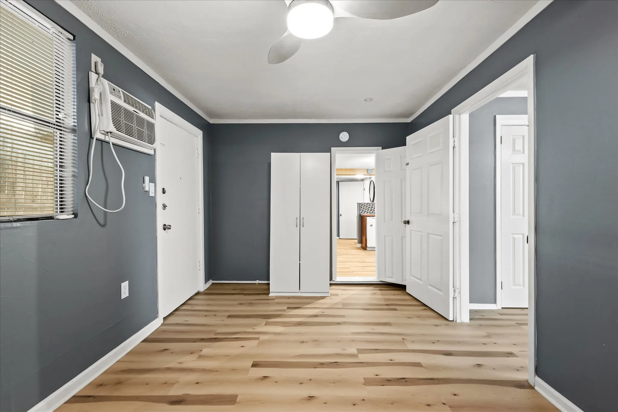 Wood-finish flooring, white trim, ceiling fan, window with blinds, and a built-in white cabinet