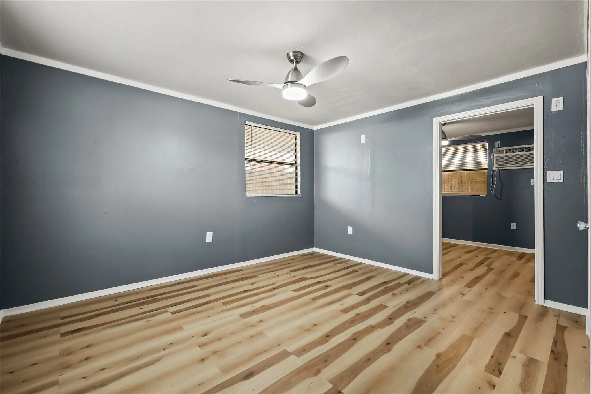 Wood-finish flooring, ceiling fan with integrated lighting, neutral wall color, and a window for natural light