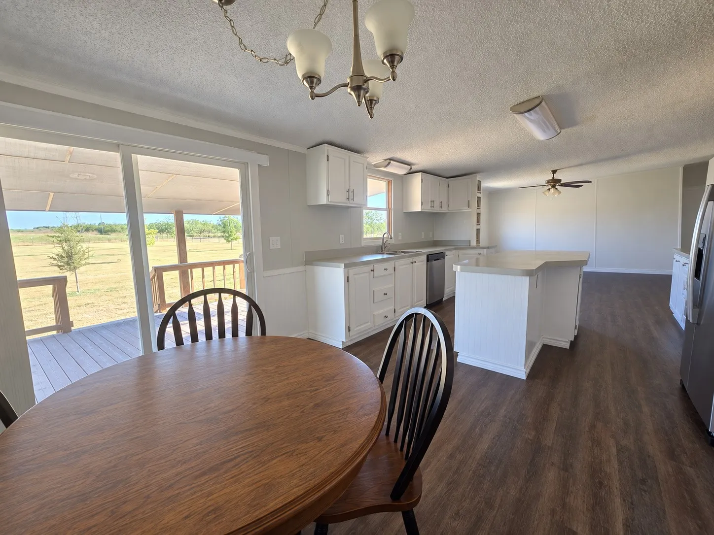Open-concept kitchen with white cabinetry and an island, stainless steel appliances, wood-finish flooring, and sliding glass doors to an outdoor deck
