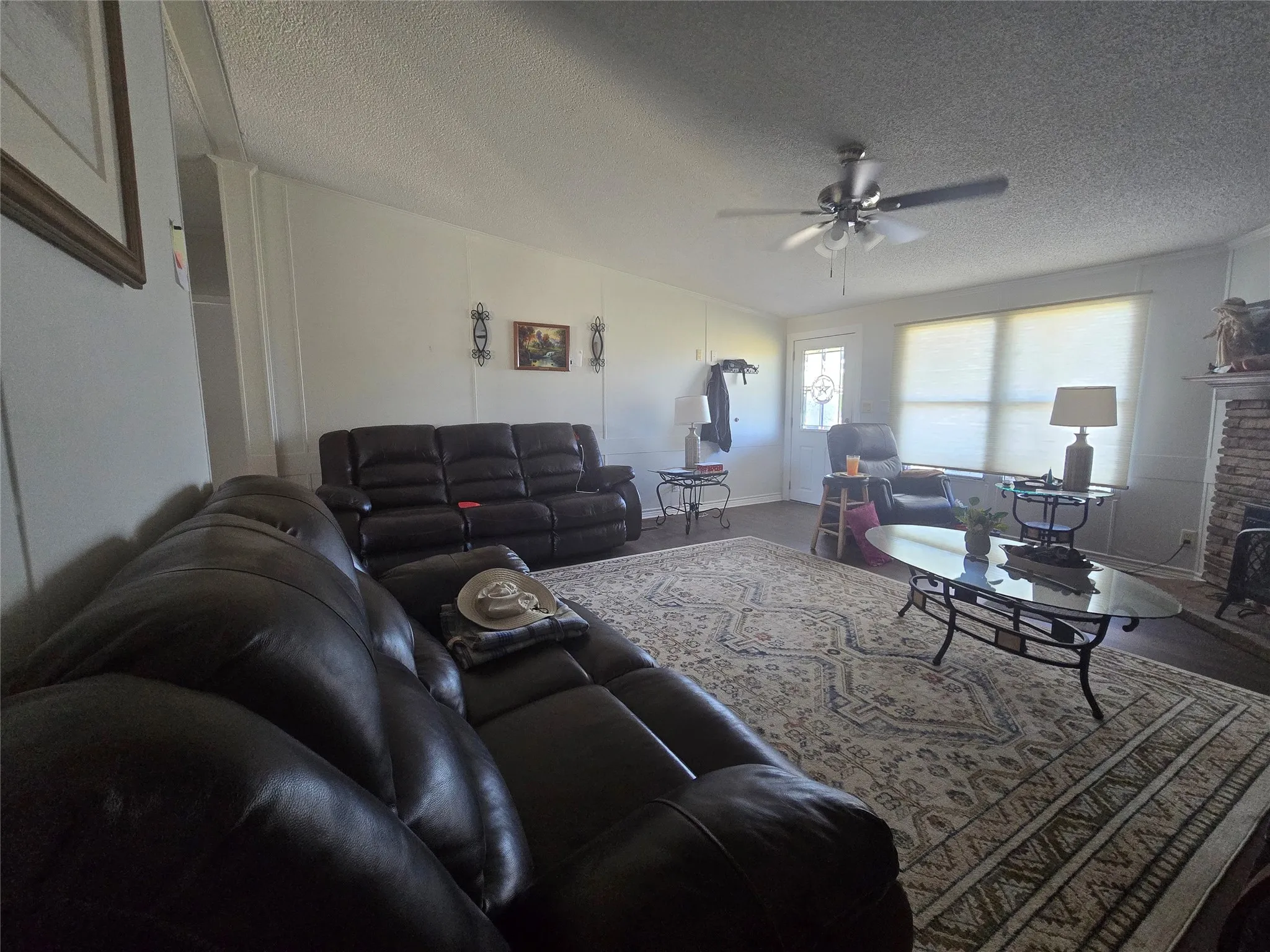 Spacious living area featuring a ceiling fan, multiple windows with blinds, and a stone-clad fireplace