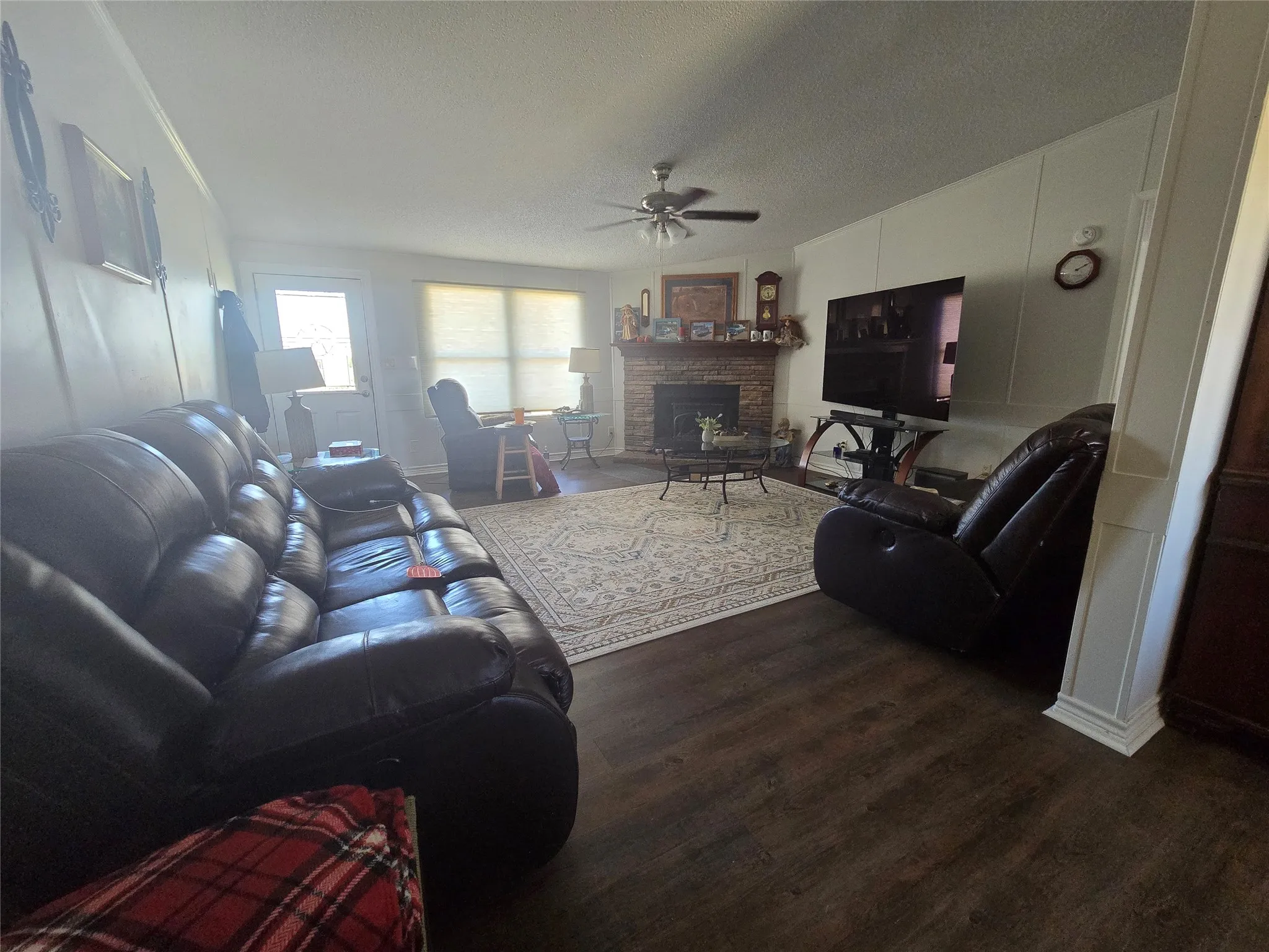 Living area featuring wood-finish flooring, a stone-surround fireplace, a ceiling fan, and paneled accent walls