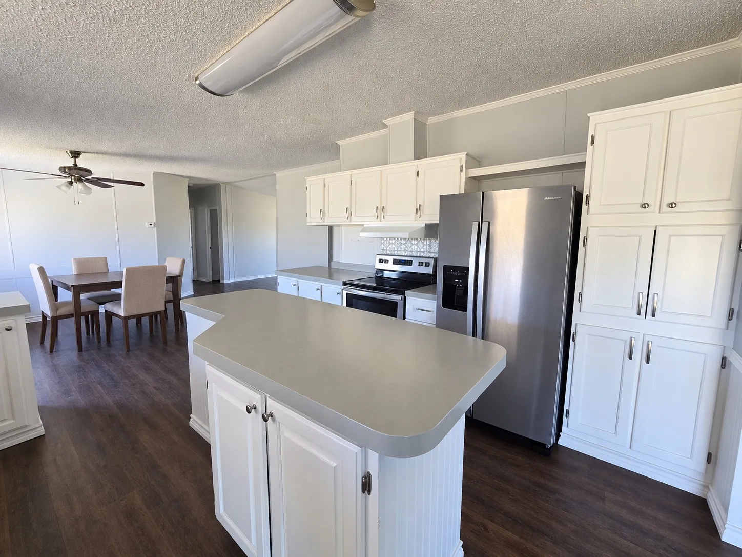 Kitchen featuring an island, white cabinetry, stainless steel appliances, and wood-finish flooring