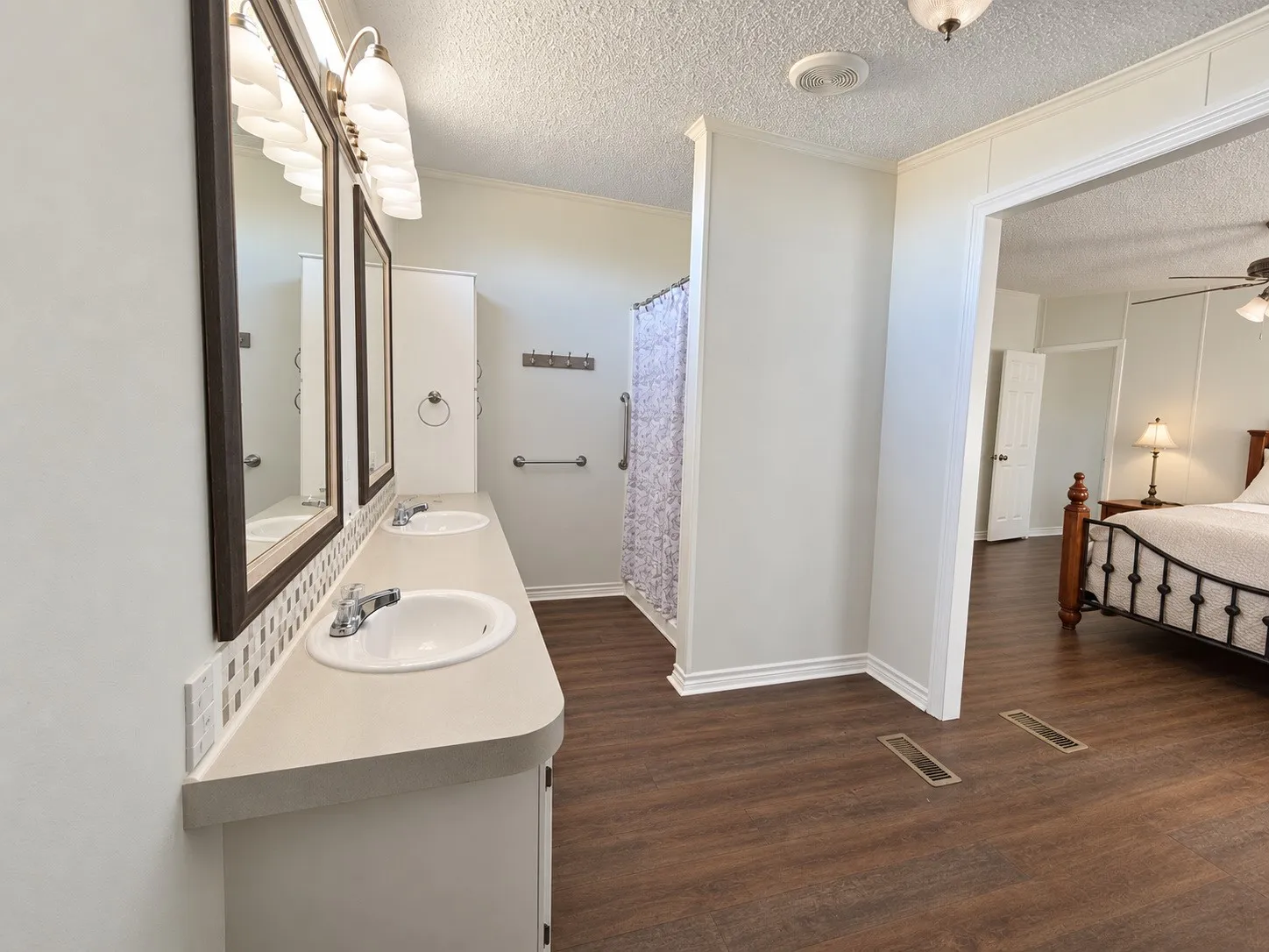Dual vanity with integrated sinks, mosaic tile backsplash, wood-finish flooring, and a built-in shower