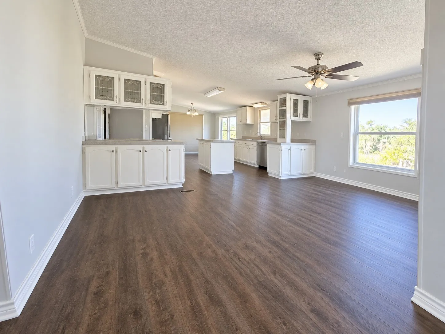 Open-concept living space featuring wood-finish flooring, white cabinetry, a kitchen island, vaulted ceilings, and a ceiling fan