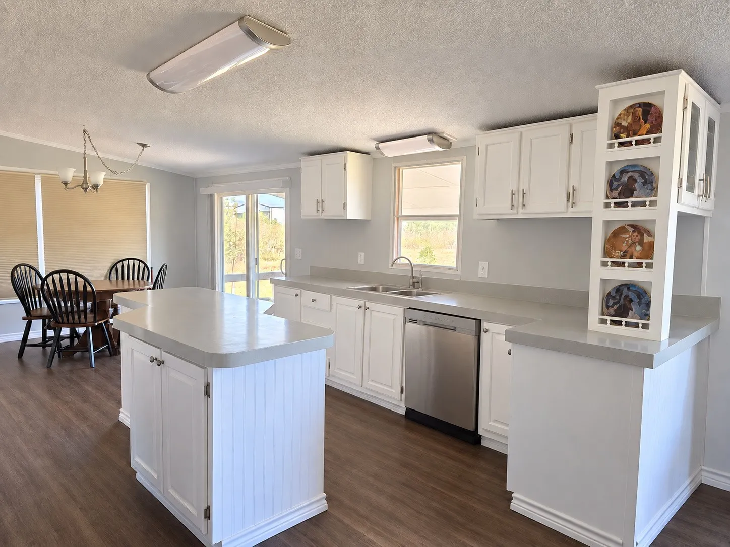 Kitchen featuring white cabinetry, light countertops, a stainless steel dishwasher, a central island, and wood-finish flooring.
