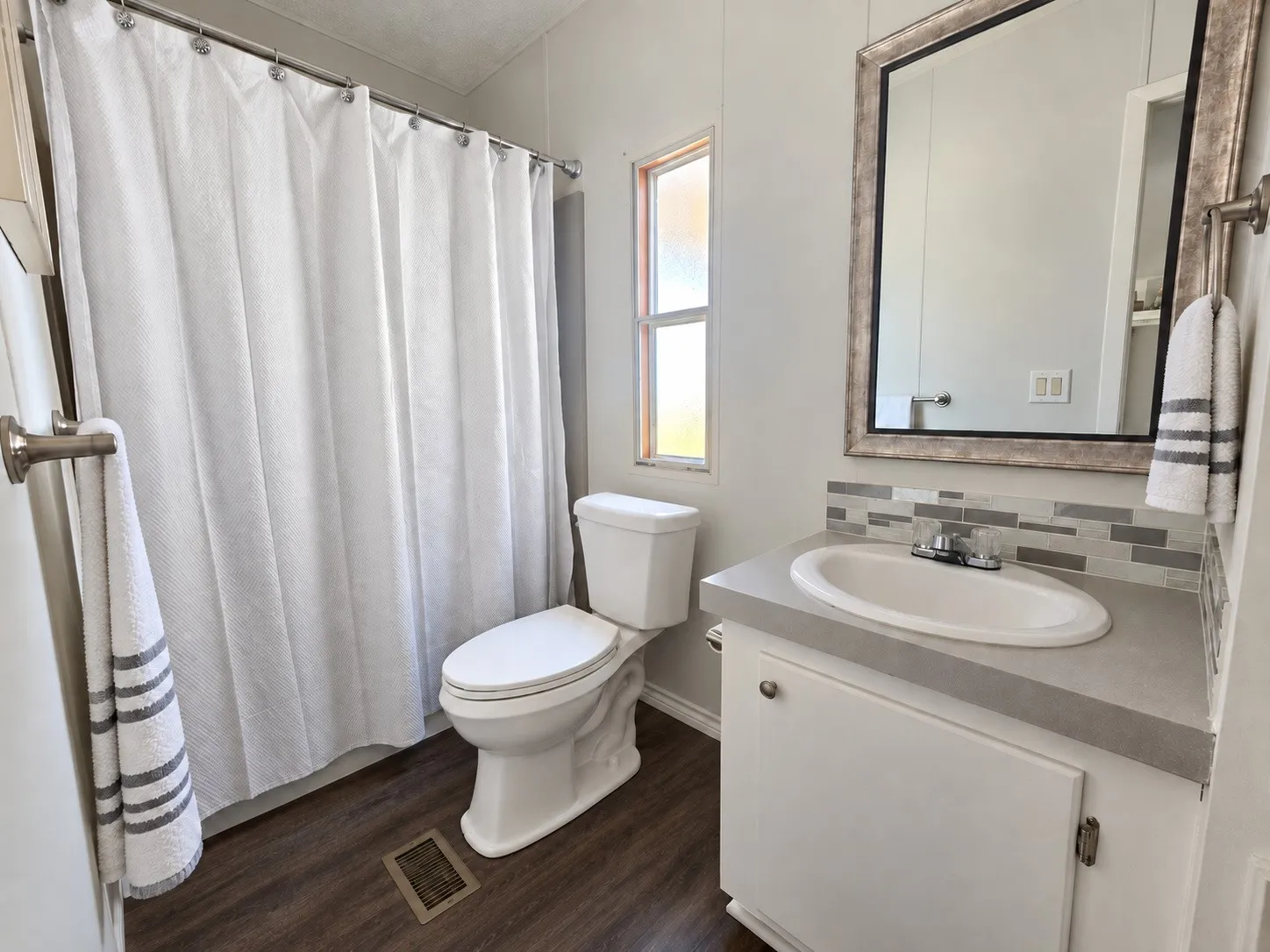 Bathroom featuring a built-in vanity with an integrated sink, mosaic tile backsplash, and dark wood-finish flooring