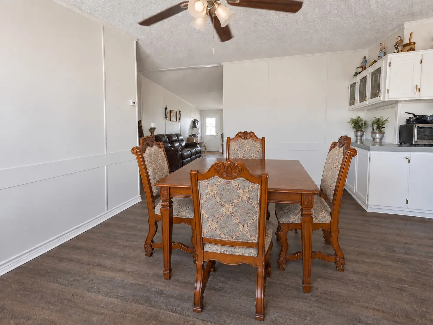 Wood-finish flooring, white paneled walls, white cabinetry with silver hardware, and a ceiling fan with integrated lighting