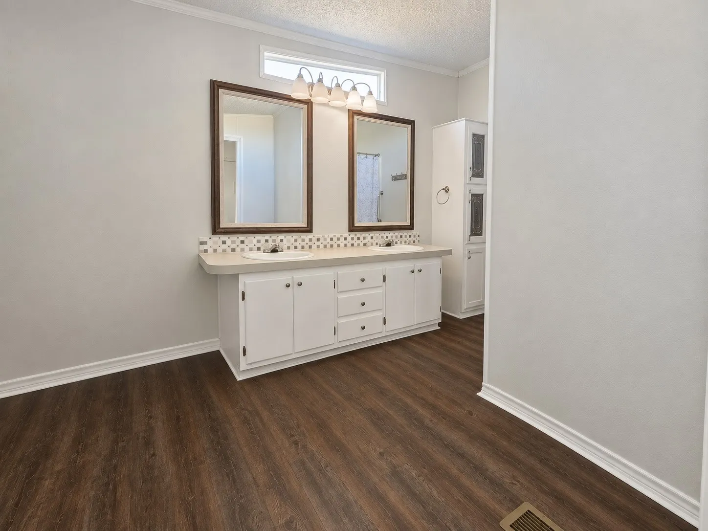 Dual vanity with recessed sinks, mosaic tile backsplash, wood-finish flooring, and integrated storage cabinetry