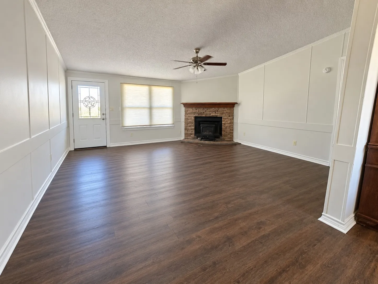 Spacious living area featuring wood-finish flooring, wainscoting, and a stone-clad fireplace