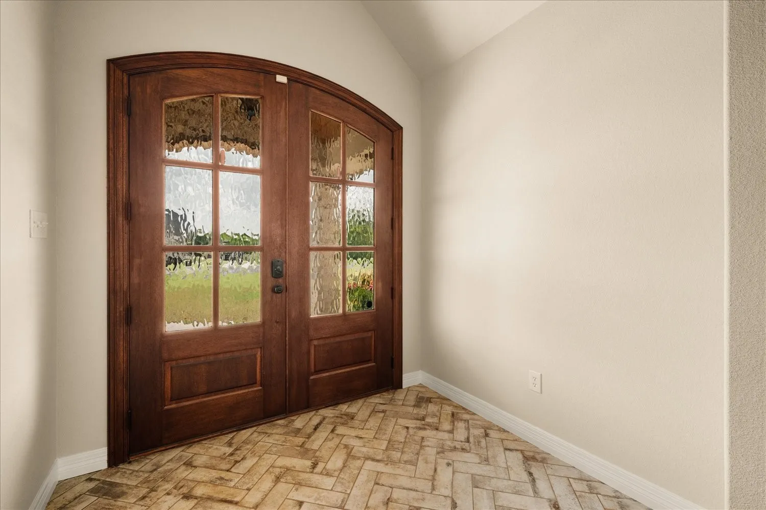 Arched double entry doors with textured glass, wood-finish flooring in a herringbone pattern, and neutral wall tones