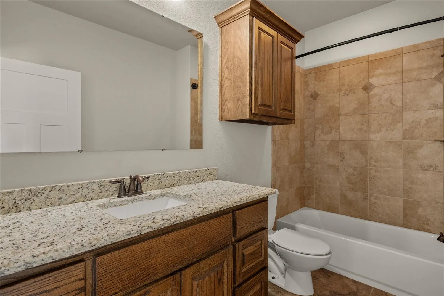 Bathroom featuring a vanity with an integrated sink, a speckled countertop, wood-finish cabinetry, and a shower-tub combination with tiled walls