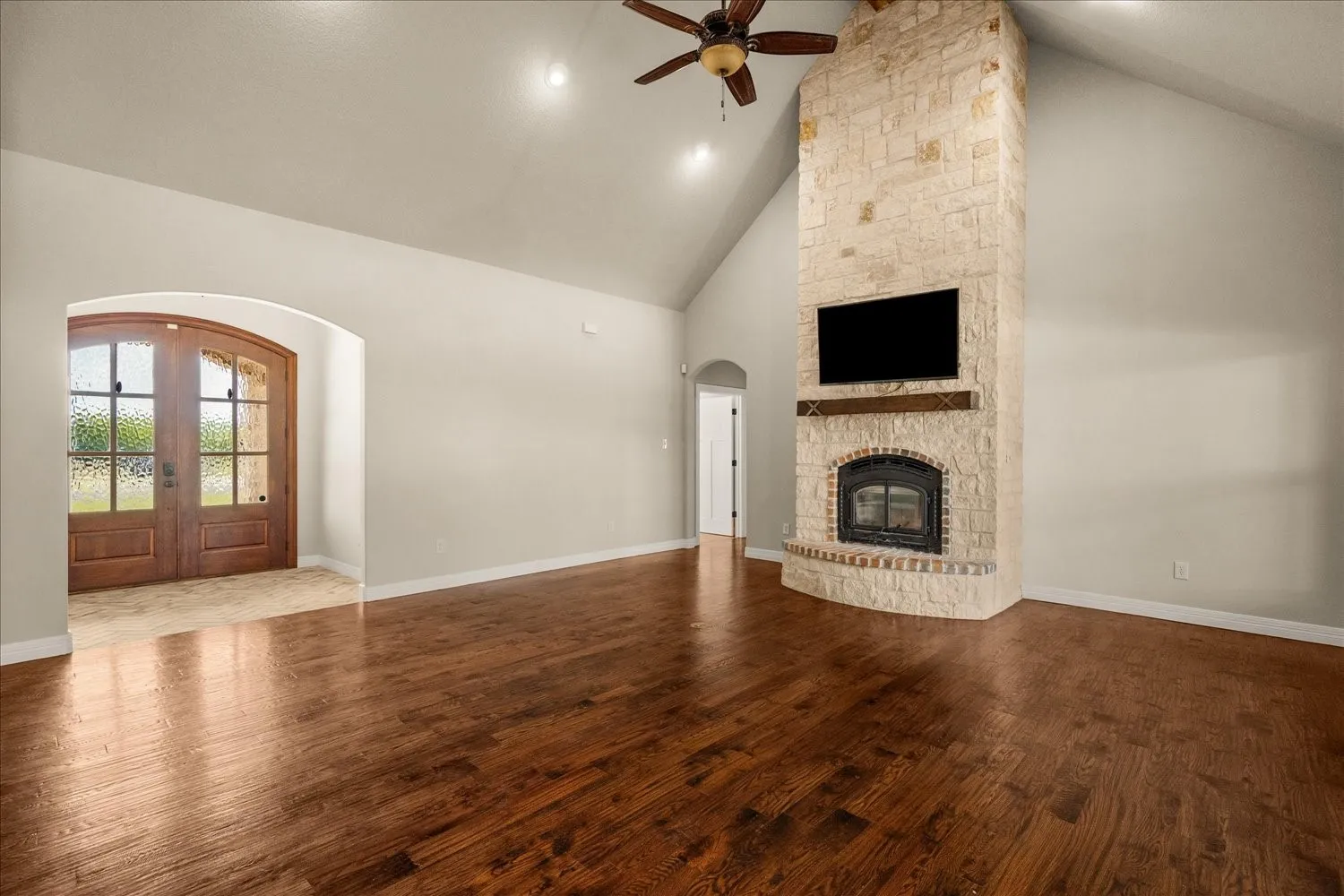 Vaulted ceiling, stone-clad fireplace, wood-finish flooring, arched doorway, and double entry doors